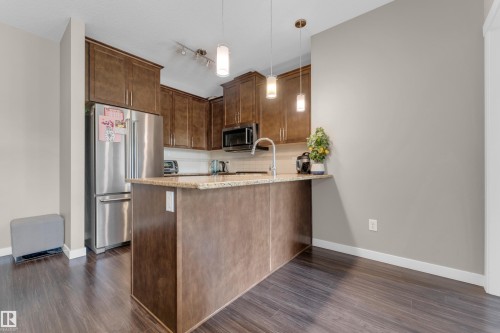 Kitchen featuring wood-finish cabinetry, stainless steel appliances, a center island with pendant lighting, a gooseneck faucet, and light-toned countertops - 115 812 Welsh Drive Sw, Edmonton, AB 