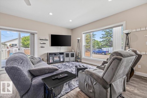 Spacious living area featuring expansive windows, wood-finish flooring, recessed lighting, a ceiling fan, and sliding glass doors opening to an exterior deck - 4708 47A Avenue, Onoway, AB 