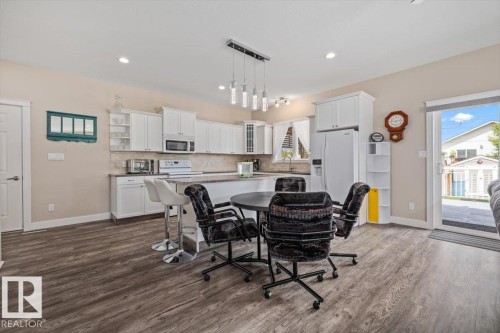 Open-concept kitchen and dining area featuring wood-finish flooring, white cabinetry, and a neutral backsplash - 4708 47A Avenue, Onoway, AB 