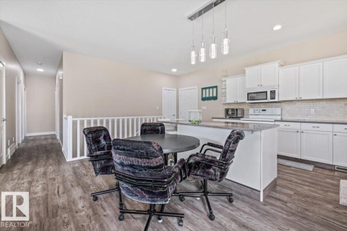 Open-concept kitchen featuring white cabinetry, stone countertops, a subway tile backsplash, and a central island with pendant lighting - 4708 47A Avenue, Onoway, AB 