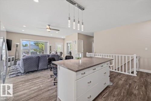 Expansive open-concept living area featuring wood-finish flooring, a kitchen island with stone countertop, and a contemporary linear pendant light fixture - 4708 47A Avenue, Onoway, AB 