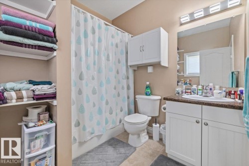 Bathroom featuring a single vanity with a laminate countertop, a mirrored medicine cabinet, a full bathtub with shower, and built-in shelving - 4708 47A Avenue, Onoway, AB 