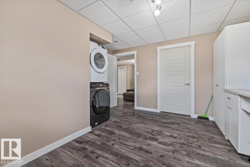 Laundry area featuring a stacked washer and dryer, wood-finish flooring, and white cabinetry with a countertop - 4708 47A Avenue, Onoway, AB 