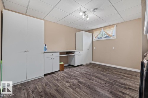 Dedicated utility space featuring extensive built-in white cabinetry, a built-in countertop with open shelving, wood-finish flooring, and a drop ceiling with recessed lighting - 4708 47A Avenue, Onoway, AB 