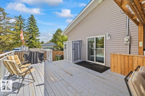Expansive exterior deck featuring a grey wood-finish surface, white railings, and a sliding glass door - 4708 47A Avenue, Onoway, AB 