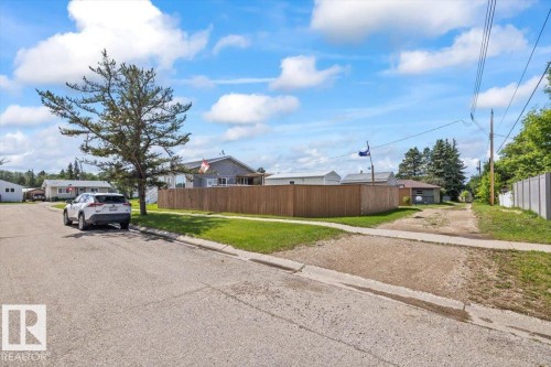 Expansive lot featuring a wooden privacy fence, mature trees, a gravel parking area, and a paved street frontage - 4708 47A Avenue, Onoway, AB 