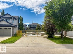 Residential lot featuring a concrete driveway and sidewalk, surrounded by established trees and green spaces - 