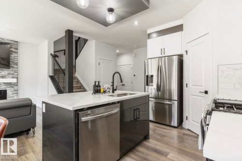 Modern kitchen island featuring a white countertop, undermount sink, and integrated stainless steel dishwasher - 19703 29 Avenue, Edmonton, AB 