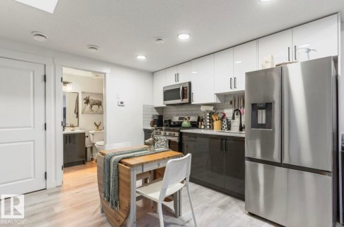 Contemporary kitchen featuring white upper cabinetry, dark lower cabinetry, and light wood-finish flooring - 19703 29 Avenue, Edmonton, AB 
