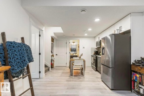 Kitchen area featuring light wood-finish flooring, white flat-panel cabinetry, stainless steel appliances, recessed lighting, and a subway tile backsplash - 19703 29 Avenue, Edmonton, AB 