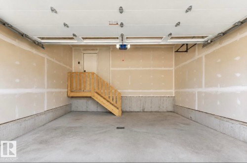 Spacious garage featuring a concrete floor, unpainted drywall walls, and a built-in wooden staircase - 19703 29 Avenue, Edmonton, AB 