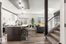 Open-concept interior featuring a kitchen with white upper cabinetry and a dark gray island, stainless steel appliances, and wood-finish flooring - 19703 29 Avenue, Edmonton, AB 