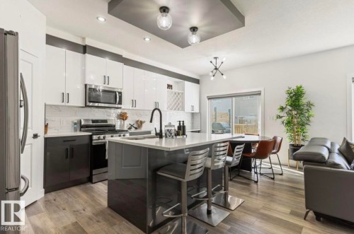 Contemporary kitchen featuring two-tone cabinetry, stainless steel appliances, a central island with integrated seating, and wood-finish flooring - 19703 29 Avenue, Edmonton, AB 