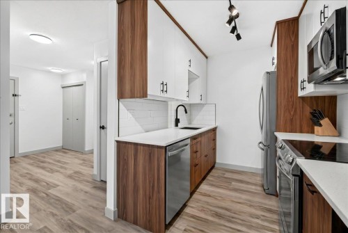 Modern kitchen featuring stainless steel appliances, wood-finish lower cabinetry, white upper cabinetry with matte black hardware, and a subway tile backsplash - Edmonton, AB 