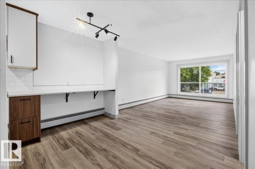Spacious room featuring wood-finish flooring, a large window, and a built-in desk area with white subway tile backsplash and dark wood-finish cabinetry - Edmonton, AB 