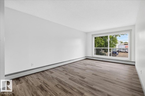 Bright room featuring a large picture window, wood-finish flooring, white walls, and baseboard heating - Edmonton, AB 