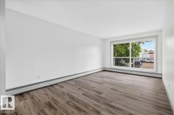 Bright room featuring a large picture window, wood-finish flooring, white walls, and baseboard heating - 