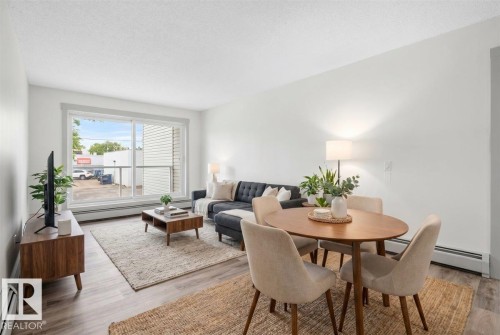 Open-concept living area featuring wood-finish flooring, a large sliding glass door, white walls, and baseboard heating - Edmonton, AB 