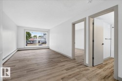 Spacious interior showcasing wood-finish flooring, white walls, and a large window - 