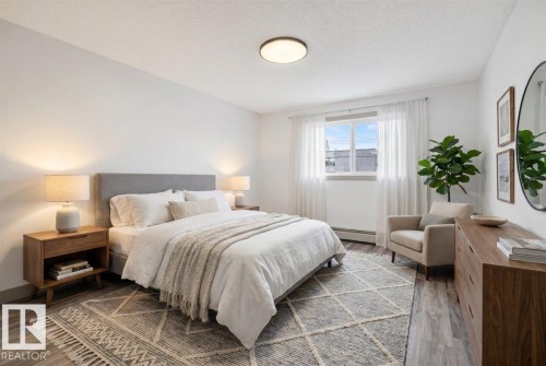 Bright bedroom featuring a large window, contemporary ceiling light fixture, wood-finish flooring, and a textured area rug - Edmonton, AB 