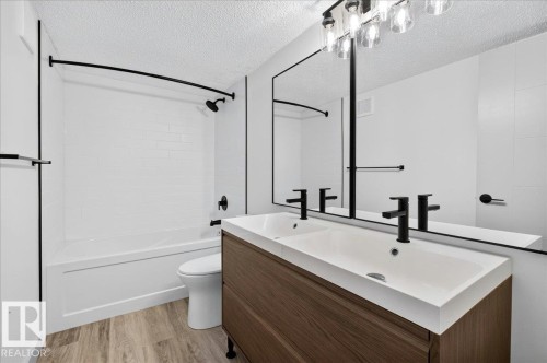 Bathroom featuring a dual-sink vanity with wood-finish cabinetry, a full-width mirror, and matte black fixtures - Edmonton, AB 
