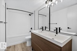 Bathroom featuring a dual-sink vanity with wood-finish cabinetry, a full-width mirror, and matte black fixtures - 