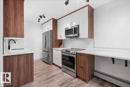 Modern kitchen featuring two-tone cabinetry, stainless steel appliances, a white subway tile backsplash, white countertops, and wood-finish flooring - Edmonton, AB 