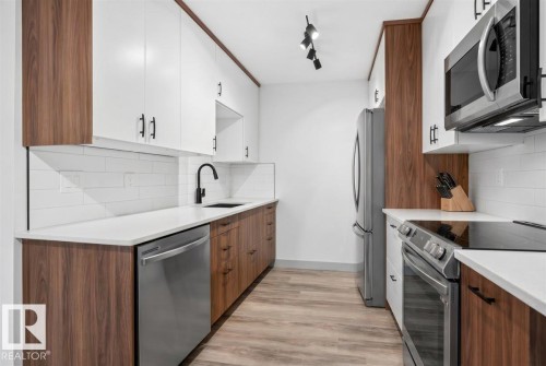 Modern kitchen with two-tone cabinetry, stainless steel appliances, white subway tile backsplash, and light wood-finish flooring - Edmonton, AB 