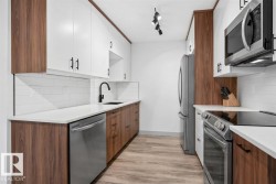 Modern kitchen with two-tone cabinetry, stainless steel appliances, white subway tile backsplash, and light wood-finish flooring - 