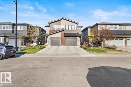 Modern duplex exterior featuring a two-tone facade, stone accents, and two individual garage doors - 2847 Koshal Crescent, Edmonton, AB - Outdoor With Facade