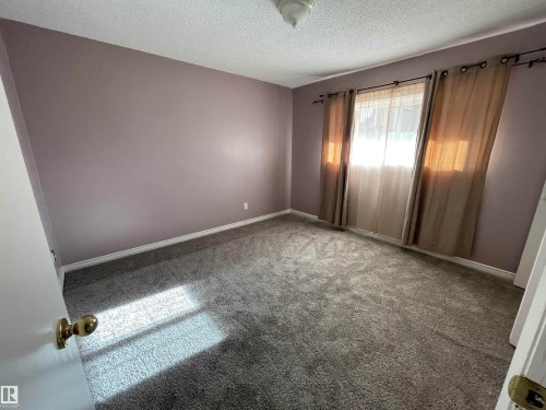 Carpeted room featuring a window with privacy drapes, a ceiling-mounted light fixture, and light purple wall paint - 8930B 144 Avenue, Edmonton, AB 
