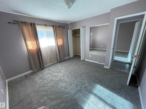 Spacious room featuring light gray carpeting, a window with drapery, a built-in closet with bifold doors, and a ceiling-mounted light fixture - 8930B 144 Avenue, Edmonton, AB 