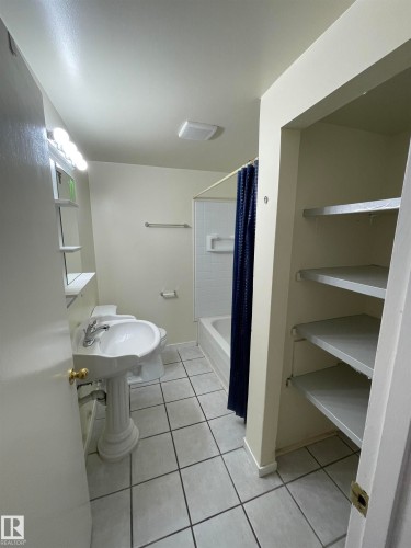 Bathroom featuring a pedestal sink, white tile flooring, built-in shelving, and a shower-tub combination - 8930B 144 Avenue, Edmonton, AB 