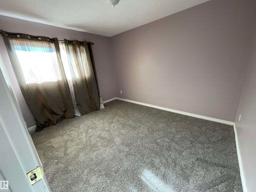 Room featuring textured grey carpeting, purple wall paint, and white baseboards - 8930B 144 Avenue, Edmonton, AB 