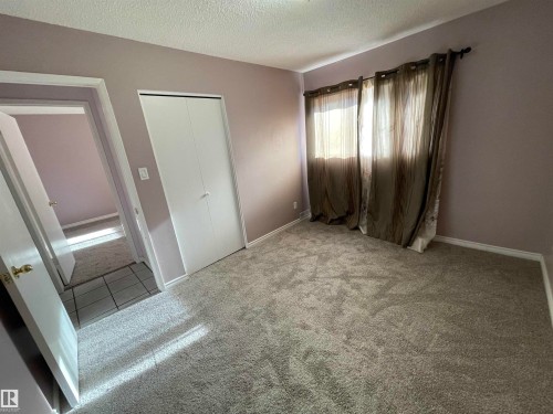Spacious room featuring neutral-toned carpeting, light purple wall paint, and white baseboards - 8930B 144 Avenue, Edmonton, AB 