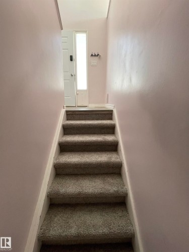 Carpeted staircase with white risers and a light-colored entry door featuring a vertical glass insert - 8930B 144 Avenue, Edmonton, AB 