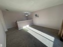 Carpeted interior space featuring a partial wall, white baseboards, and a semi-flush mount ceiling fixture - 8930B 144 Avenue, Edmonton, AB 
