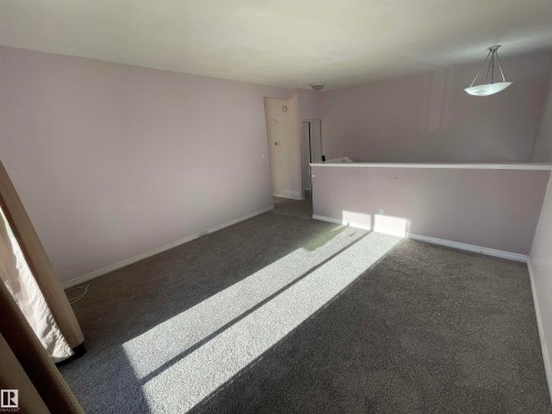 Carpeted interior space featuring light lavender walls, white baseboards, and a contemporary pendant light fixture - 8930B 144 Avenue, Edmonton, AB 