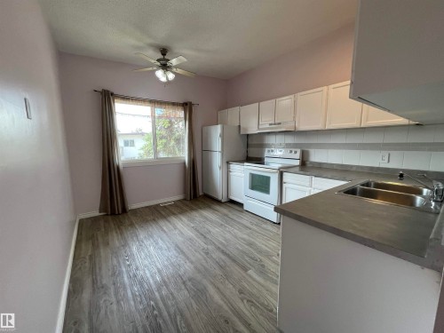 Kitchen area featuring wood-finish flooring, white cabinetry, a double basin stainless steel sink, and a ceiling fan - 8930B 144 Avenue, Edmonton, AB 