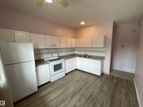 Kitchen featuring wood-finish flooring, white cabinetry, a double basin sink, and white appliances - 8930B 144 Avenue, Edmonton, AB 
