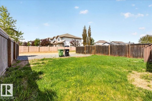 Expansive backyard featuring a green lawn, wood fencing, and a gravel pad - 150 Acacia Circle, Leduc, AB - Outdoor With Backyard
