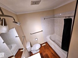 Bathroom featuring a white bathtub, tiled shower surround, and rich wood-finish flooring - 