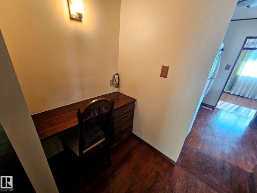 Built-in wood-finish desk with storage drawers, complemented by a sconce lighting fixture and wood-finish flooring - 7612 40 Avenue Nw, Edmonton, AB - Indoor Photo Showing Other Room