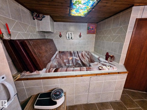 Indoor spa tub with a patterned interior, surrounded by light gray geometric wall tiling and a wood-finish ceiling - 7612 40 Avenue Nw, Edmonton, AB - Indoor