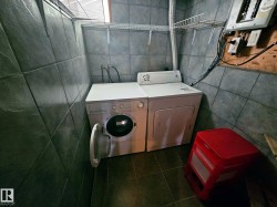 Dedicated laundry area featuring slate-look tile flooring and walls, built-in wire shelving, and overhead window with blinds - 