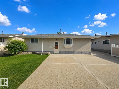 Exterior featuring a bay window, a concrete driveway, a manicured lawn, and a light-colored stucco finish with a stone-look foundation - 7612 40 Avenue Nw, Edmonton, AB - Outdoor