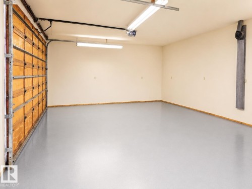 Spacious garage featuring a light gray epoxy floor coating, light beige walls, and natural wood baseboards - 7612 40 Avenue Nw, Edmonton, AB - Indoor