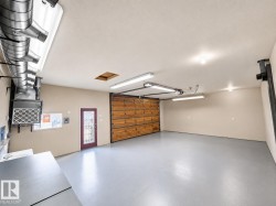Spacious garage featuring a light gray epoxy floor, wood-panel garage door, and a burgundy entry door with decorative glass - 