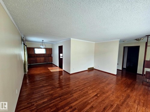 Spacious room with wood-finish flooring, light-toned walls, and white crown molding - 7612 40 Avenue Nw, Edmonton, AB - Indoor Photo Showing Other Room