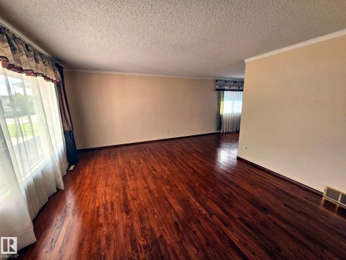 Spacious room featuring rich wood-finish flooring, light neutral-toned walls, and white crown molding - 7612 40 Avenue Nw, Edmonton, AB - Indoor Photo Showing Other Room